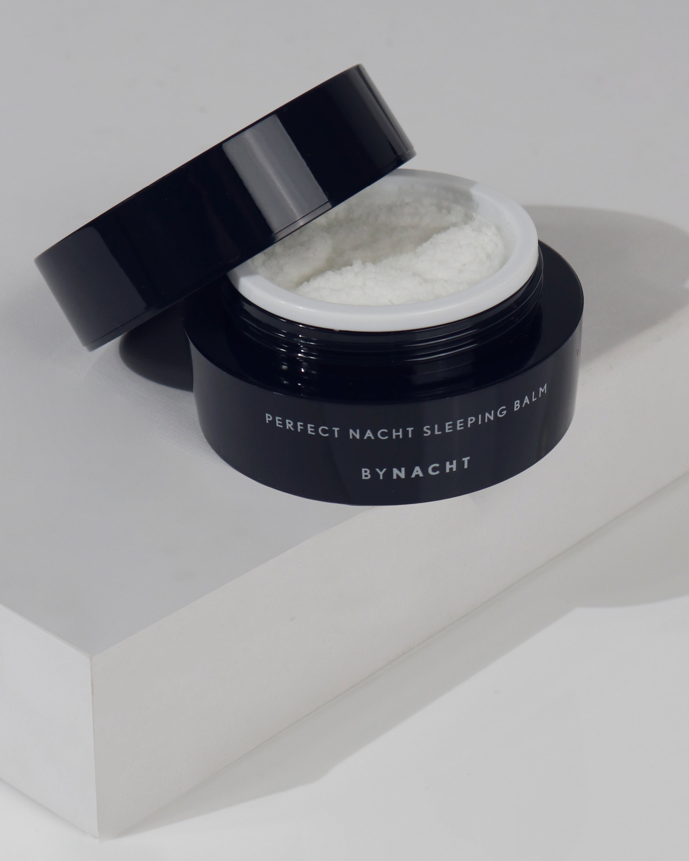 Schlaffördender Balsam im geöffneten Tiegel, der Deckel liegt diagonal auf, der Tiegel steht auf einem weißen Podest